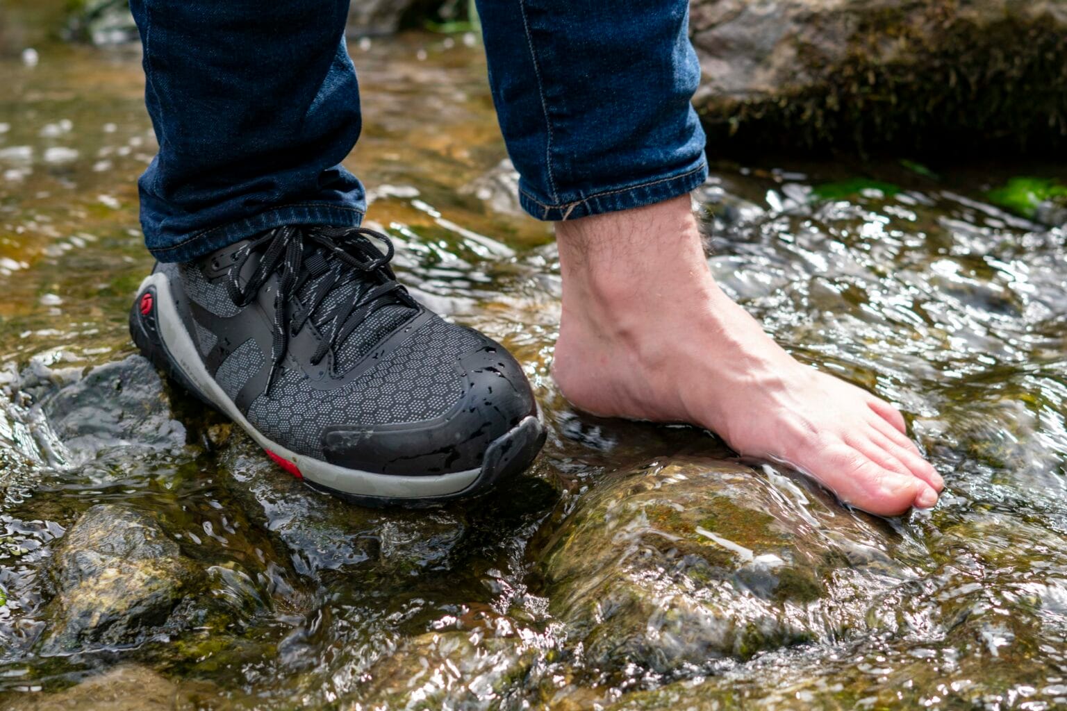 Baak Phoenix S3S Barfuss-Sicherheitsschuh, getragen in einem Bachbett; der zweite Fuss steht barfuss im Wasser